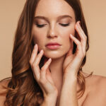 Close up Beauty portrait of sensual ginger woman with long hair posing with arms near the face over cream background